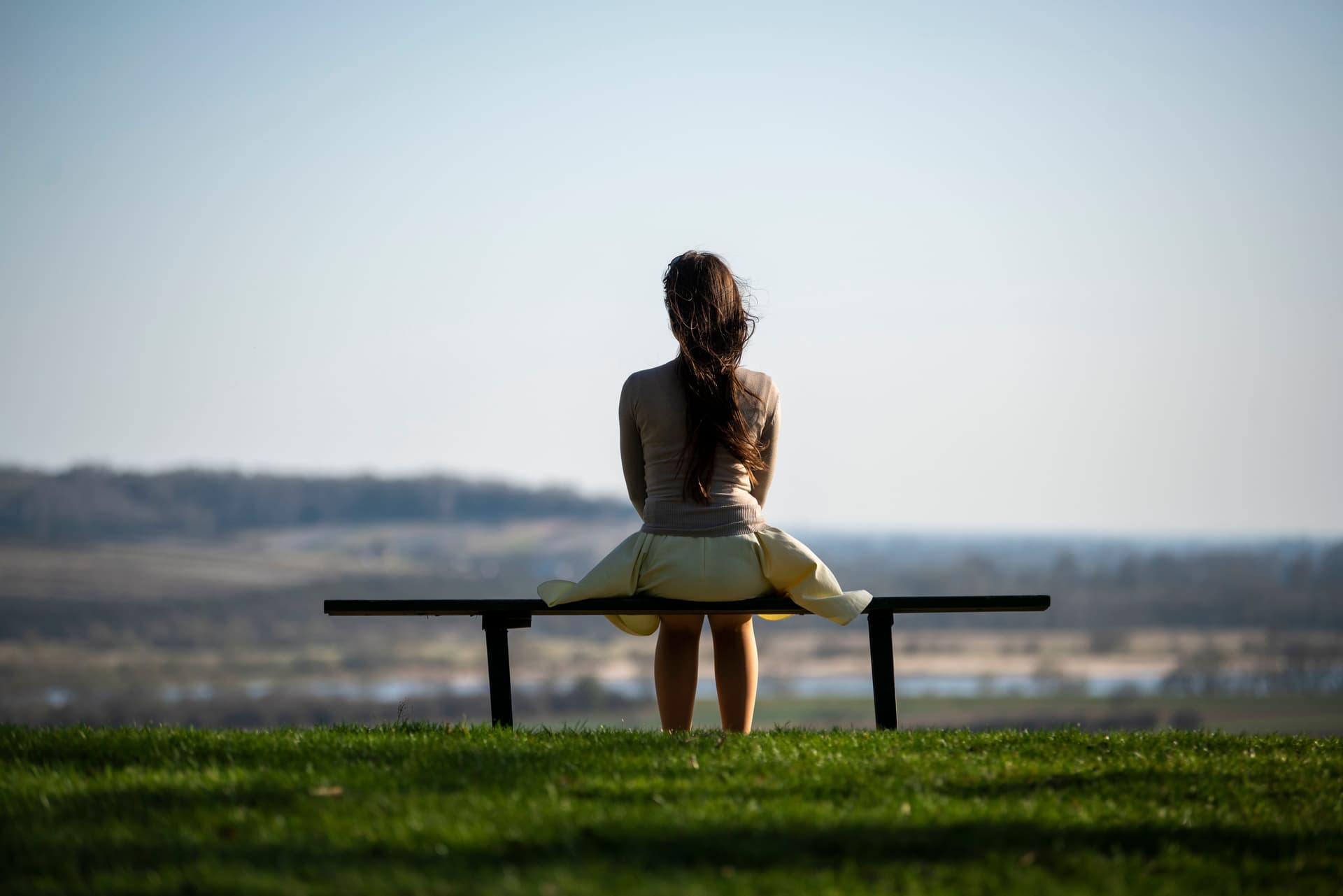 Woman sitting alone on a bench overlooking an open landscape